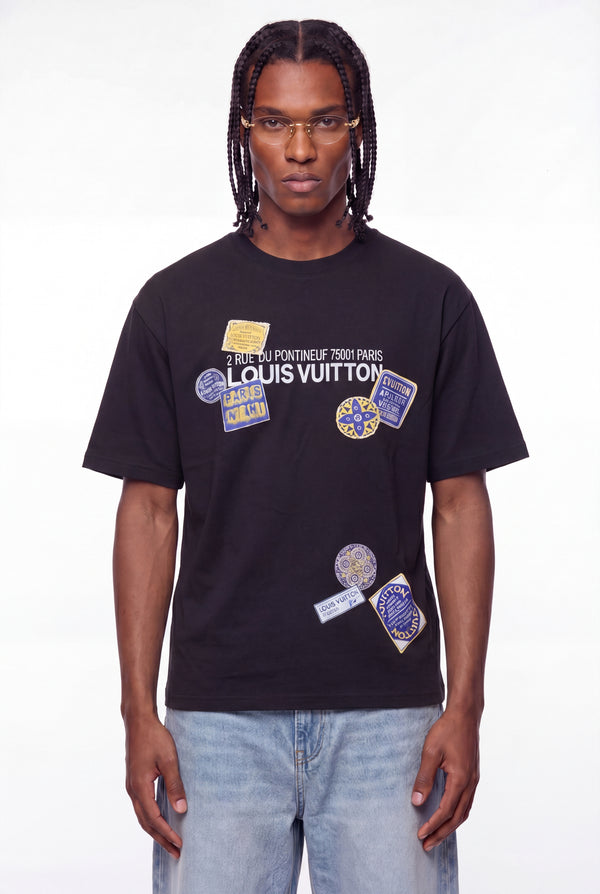 Person wearing a black Louis Vuitton t-shirt with various patches on a white background
